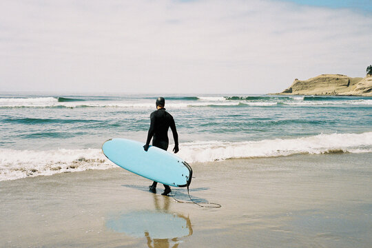 Male surfer carrying his surfboard on the beach in Pacific City