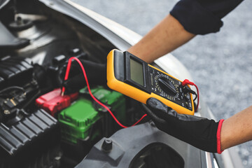 Hand car mechanic holding voltmeter to check voltage car battery energy problem for service maintenance and re charger or jump start or change battery replacement. - obrazy, fototapety, plakaty