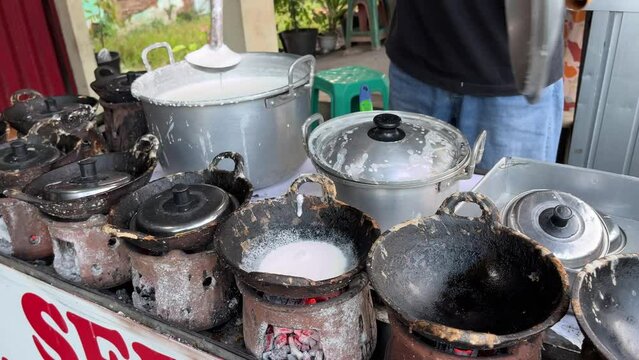 The process of making traditional dessert named Serabi made from rice flour and coconut milk by an old man with charcoal stove