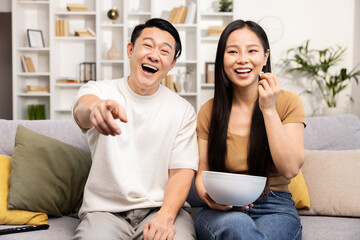 Asian couple movie night. An affectionate Asian couple relaxing on a couch with a bowl of snacks,...