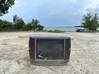 Damaged and broken television left on the road with lake and blue sky on the background