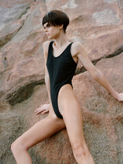 Exquisite Summer Sensation: Bikini-clad Woman Posing Happily on a Rock, Embracing Nature's Beauty by the Sea.