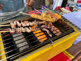 Indonesian street food vendor selling grilled squid and sausage on a hot grilling machine in a...