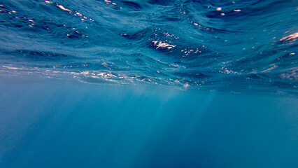 Sun rays under water. The sun's rays pass through waves on the surface of the ocean. Sun rays in the thickness of transparent water on a blue background.