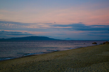 Fototapeta na wymiar Sea and sandy beach at dusk. View of the beach, calm sea and tropical island on the horizon in the evening.