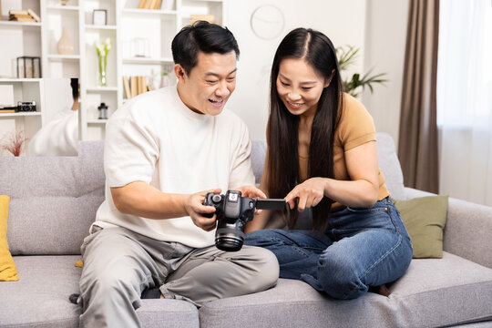 A joyful couple sits on the sofa, reviewing photos on a digital camera, sharing a light-hearted moment in a cozy home setting.