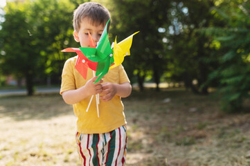 A 3-4 year old boy hides his eyes behind colorful pinwheels. The child is shy. The child does not...