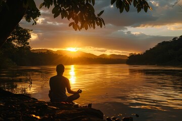 Tranquil scene of a person meditating beside a calm river at sunset, casting a serene silhouette - 784316307