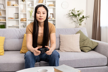 A serene young woman with headphones plays a video game while sitting comfortably on her living room couch.