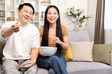 A relaxed couple sits on their comfy sofa, watching television and snacking in a cozy living room setting.