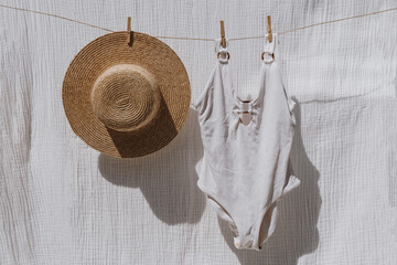 Female swimwear and straw hat hanging over white cotton cloth with strong shadows. Sunbathing on a...