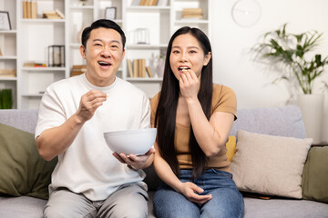 A smiling couple sitting on a couch, sharing a bowl of snacks in a cozy living room setting