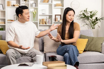 An adult couple engages in a serious discussion, sitting on their home couch, expressing emotions and resolving issues.