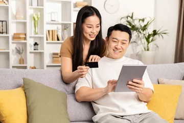 Foto op Canvas Online shopping, couple sitting on sofa with credit card and digital tablet in a cozy living room. © puhhha