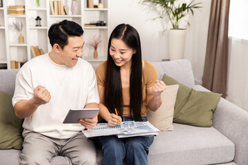 Couple Celebrating Financial Success. An Asian couple exudes joy while reviewing financial charts at home, celebrating their successful planning.