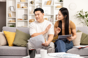 Couple budgeting at home, woman with tablet comforting worried man with bills, modern living room interior, financial planning concept