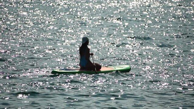 Sea woman sup. Silhouette of happy positive young woman in blue bikini, surfing on green SUP board through calm water surface. Idyllic sunset. Active lifestyle at sea or river. Slow motion