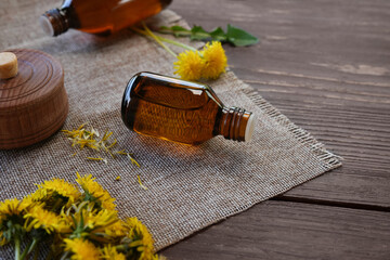 Dandelion root oil, tincture with fresh flowers and leaves on wooden table.  Green medicine,...