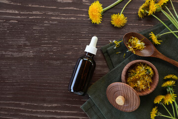 Bottle of essential oil of dandelions on wooden background. Medicinal plants and herbs composition....