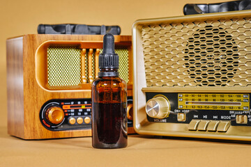 Blank amber glass essential oil bottle with retro vintage radio on brown background. Skin care concept with natural cosmetics