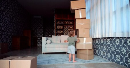 In this playful scene at home, young boy engages in game with tower of cardboard boxes. As he pulls bottom box, whole tower tumbles down in slow motion, creating unexpected cascade.