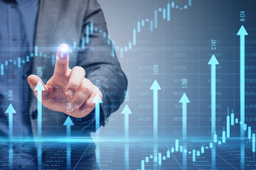 Close up of male hand pointing at growing blue vertical arrows and candlestick forex chart on...