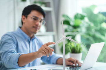 A man is pointing at a wind turbine on a laptop. He is wearing glasses and is looking at the...