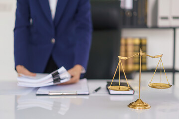Lawyer woman holding document and working about business contract with brass balance scales on desk - 784335968