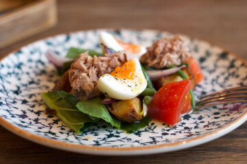 Salad with spinach, tuna, potatoes, tomatoes, onions and egg in a plate on the table