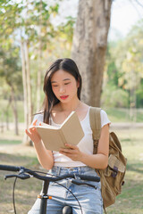 Young asian women with backpack sitting on bicycle and reading a book with happiness to resting after cycling bicycle in the nature park while relaxation with journey travel for healthy lifestyle - 784337111