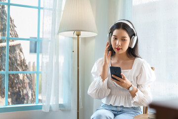 Young asian businesswoman wearing headphone to listening music and surfing social media on smartphone after analysis strategy about investment and planning of new startup project to working in cafe - 784338337