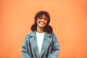 Happy African ethnicity girl with dark curly hairstyle in stylish coat looking aside and smiling