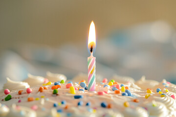 A single, lit candle on a big birthday cake, set against a light background