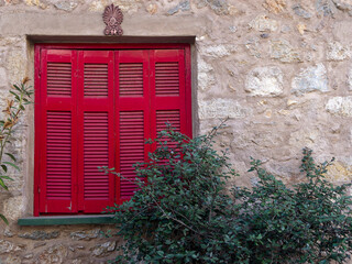 A classic design house window with bright red shutters on rough stone walls and green foliage. Travel to Athens, Greece. - 784342155