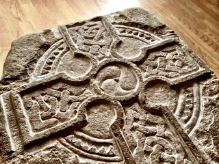 Closeup shot of the Celtic cross carved on the stone on a wooden ground