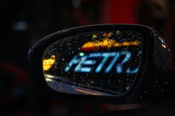Closeup shot of a car mirror with a word reflected on it, covered with raindrops, at nighttime