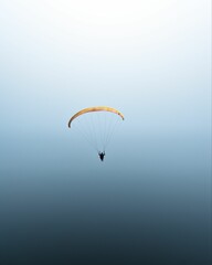 Breathtaking view of a person paragliding over the open sea in a clear cloudless sky