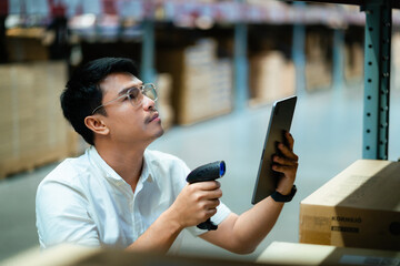 A man is looking at a tablet while holding a barcode scanner. He is in a warehouse and he is...