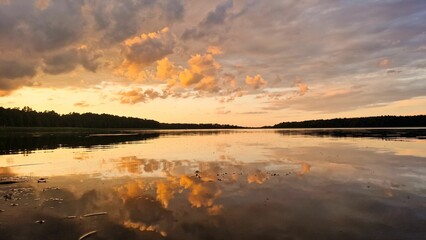 Reflection of fluffy clouds in the sunset sky on the scenic surface of a mirror lake in Poland