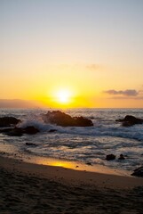 Obraz premium Red sunset view over a seascape with clear sky and sun in the background stones around