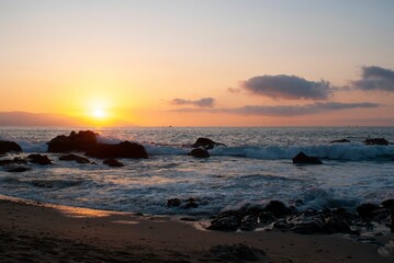 Obraz premium Red sunset view over a seascape with clear sky and sun in the background stones around