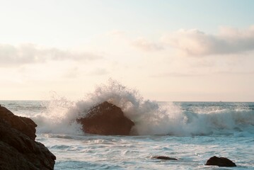 Obraz premium Seascape view with water waves hitting on rocky cliffs, sunlit sky background