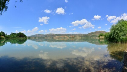 Obraz premium Beautiful lake reflecting the green trees on the shore and a cloudy sky in the background