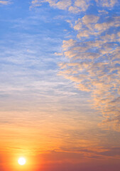 Sunset sky background in the evening with beautiful yellow sunlight and fluffy clouds on blue dusk sky in vertical frame