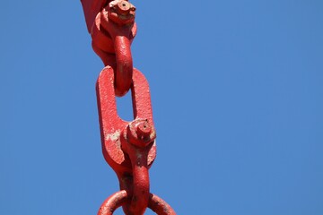 Close-up shot of a red crane chain against a blue sky in the sunlight