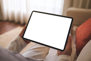 Mockup image of a woman holding digital tablet with blank desktop screen while sitting on sofa at home - 784356320
