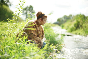 Chubby white female with ginger hair in a bun looking at a river from the shore