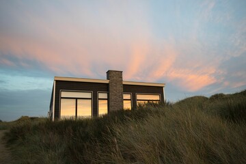 Low angle of a modern holiday house in a grass field with the colorful sky reflected in the windows