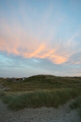 Fototapeta premium Grass terrain with houses and hills against the colorful sky during a sunset in Ringkobing, Denmark