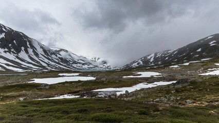 Snowy meadow against the background of mountains and cloudy sky. Norway.